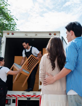 Asian Couple check while unloading boxes and furniture from a pickup truck to a new house with service cargo two men movers worker in uniform lifting boxes. concept of Home moving and delivery.